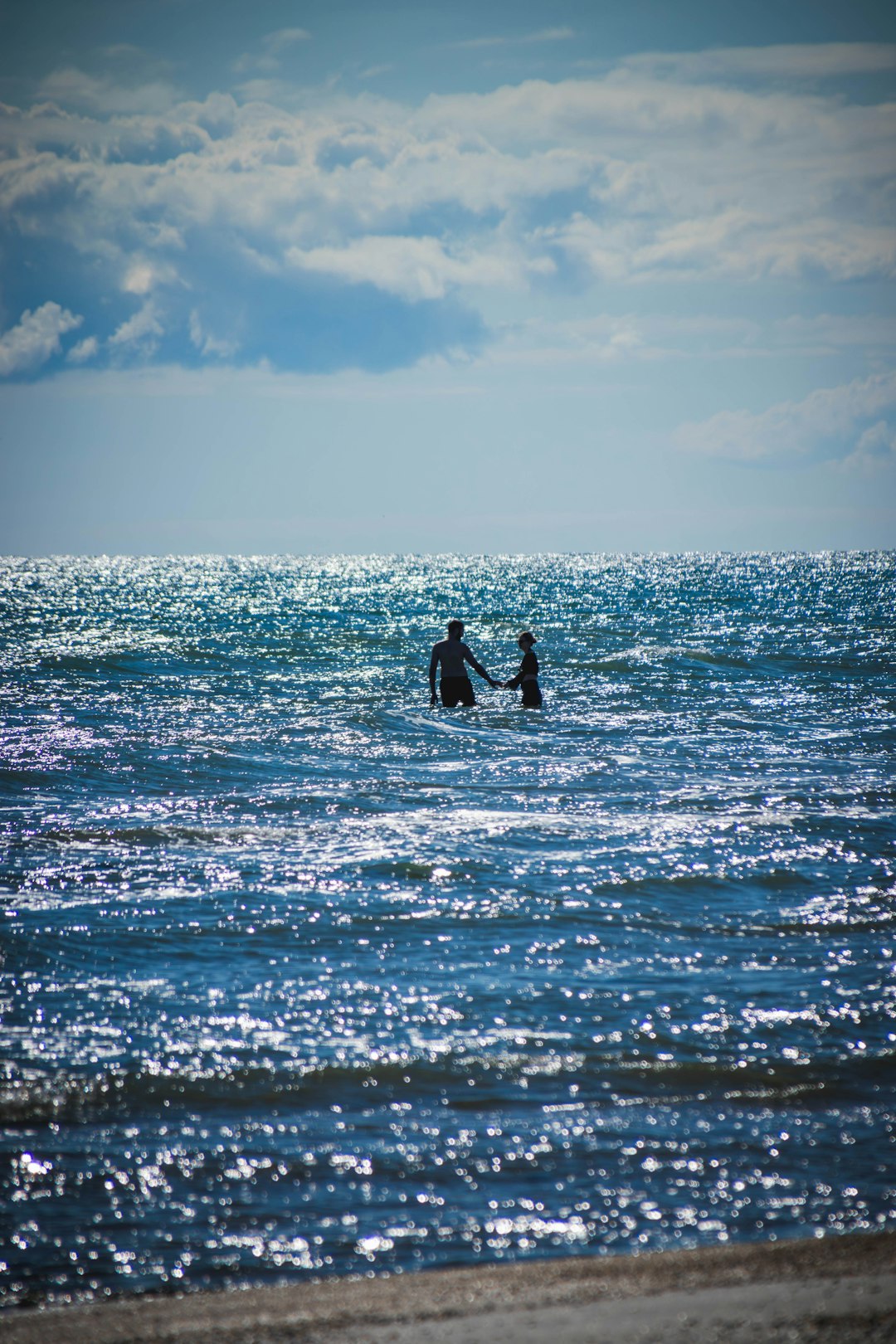 Two hands reaching toward each other over calm water beneath a cloudy sky.