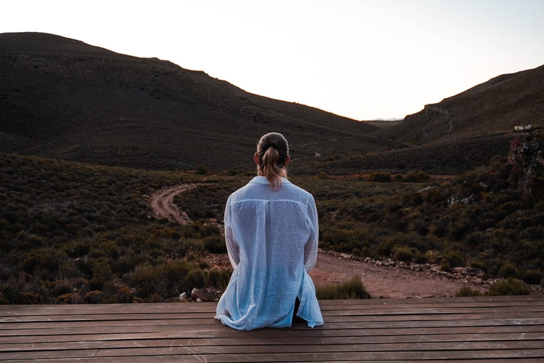 A person standing alone and looking toward a mountain landscape in soft light.
